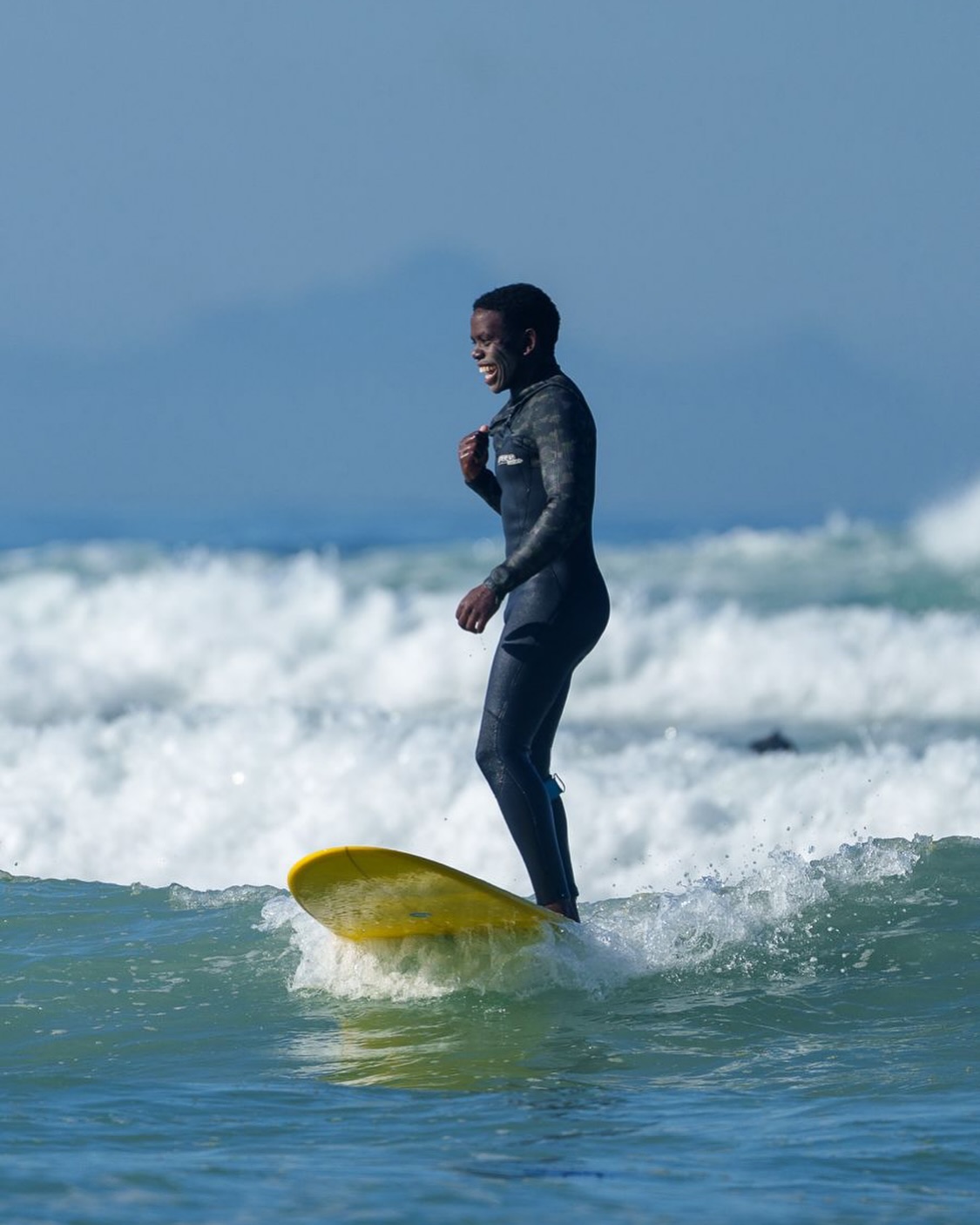 A person surfing on a yellow surfboard in the ocean at Muizenberg beach, smiling and enjoying the waves.
