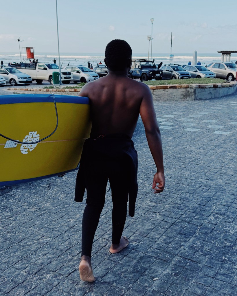 Surfer in his wetsuit going to Muizenberg beach with his surfboard