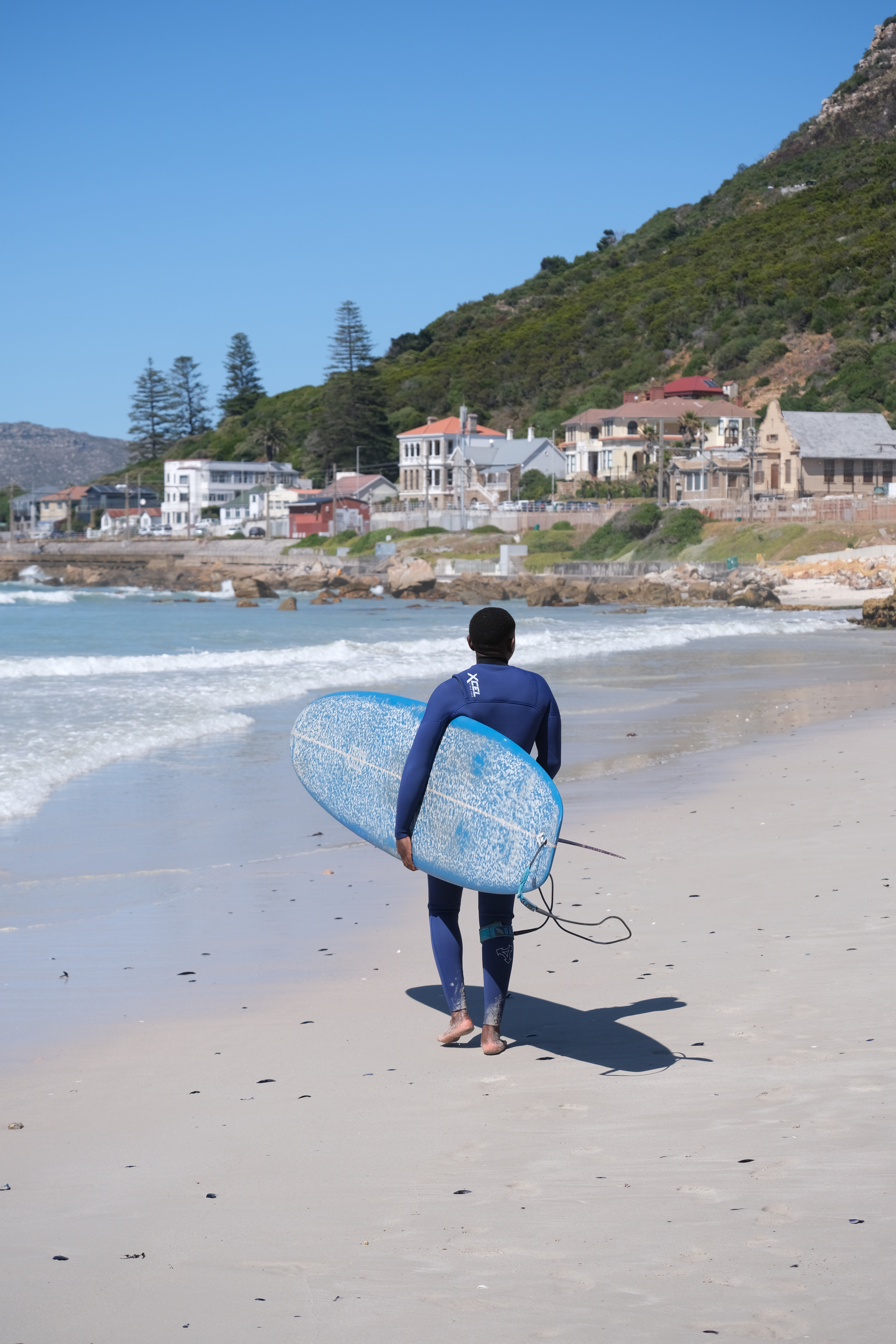 A surfer carrying his surfboard and going into the water. He is about to start a surf lesson at Muizenberg Beach in Cape Town, South Africa