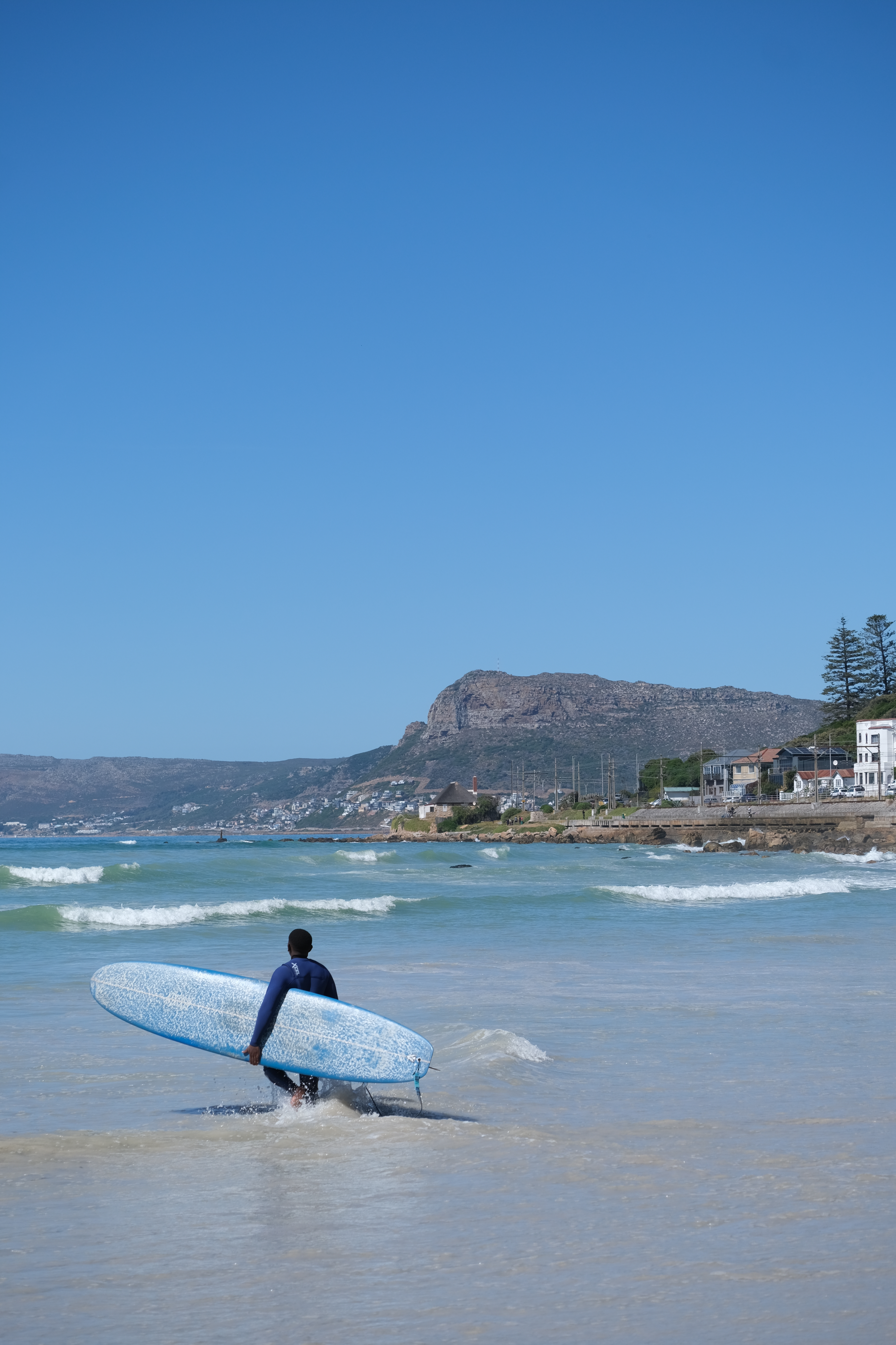 A surf coach going into the water at Muizenberg beach in Cape Town, South Africa, carrying his surfboard