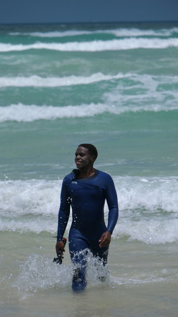 Mbuso Zozi, the surf coach of SurfXcape, getting out of the water after a surf lesson at Muizenberg Beach, Cape Town, South Africa