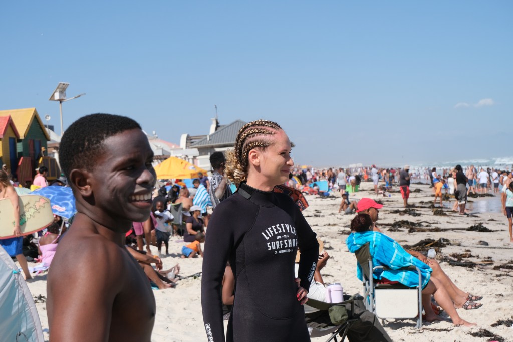 A surf coach and his beginner surf student during a lesson, looking at the waves while warming up for their surf session