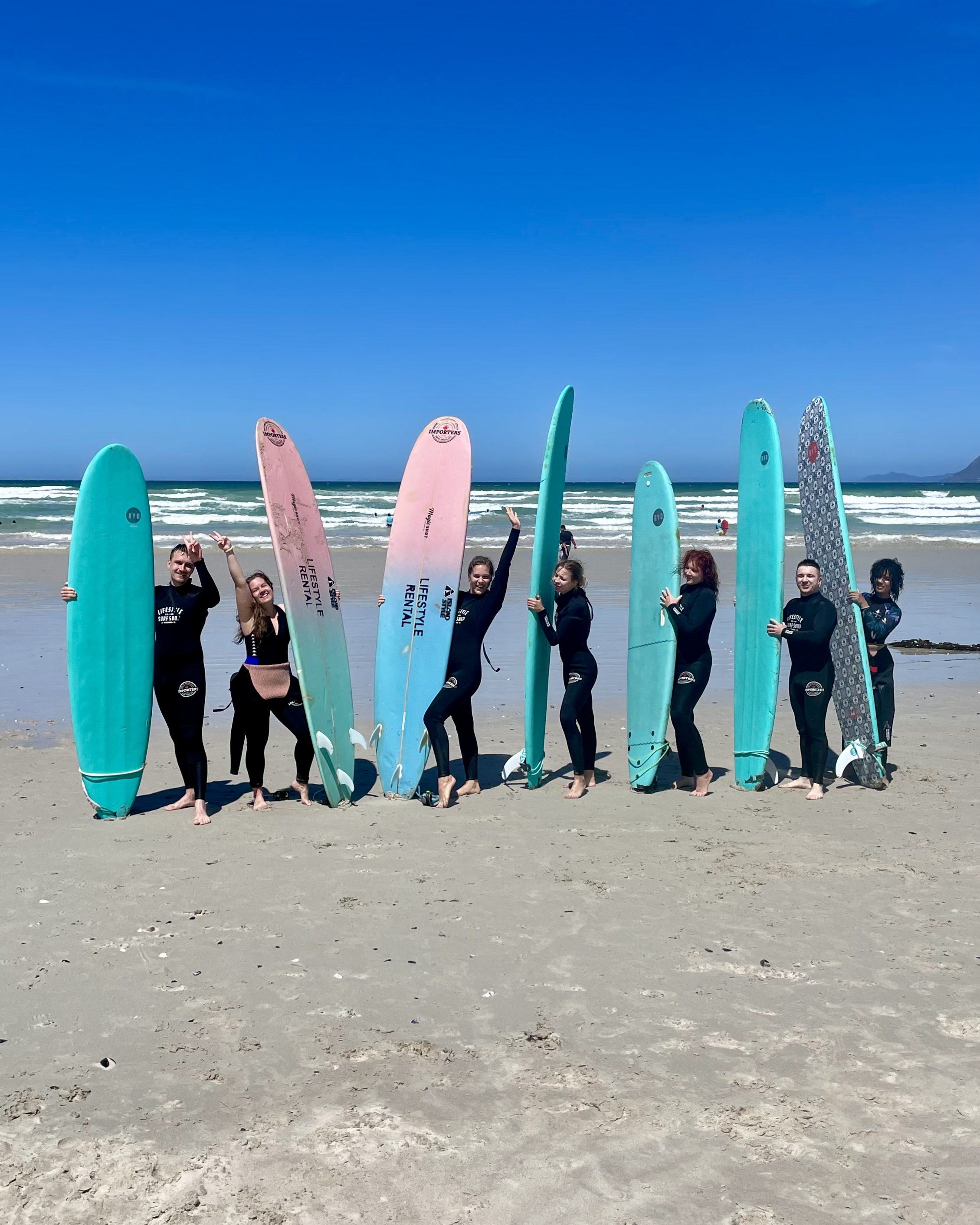 A group of beginner surfers at a group surf lesson, posing for a picture with their surfboards at Muizenberg beach in Cape Town, South Africa