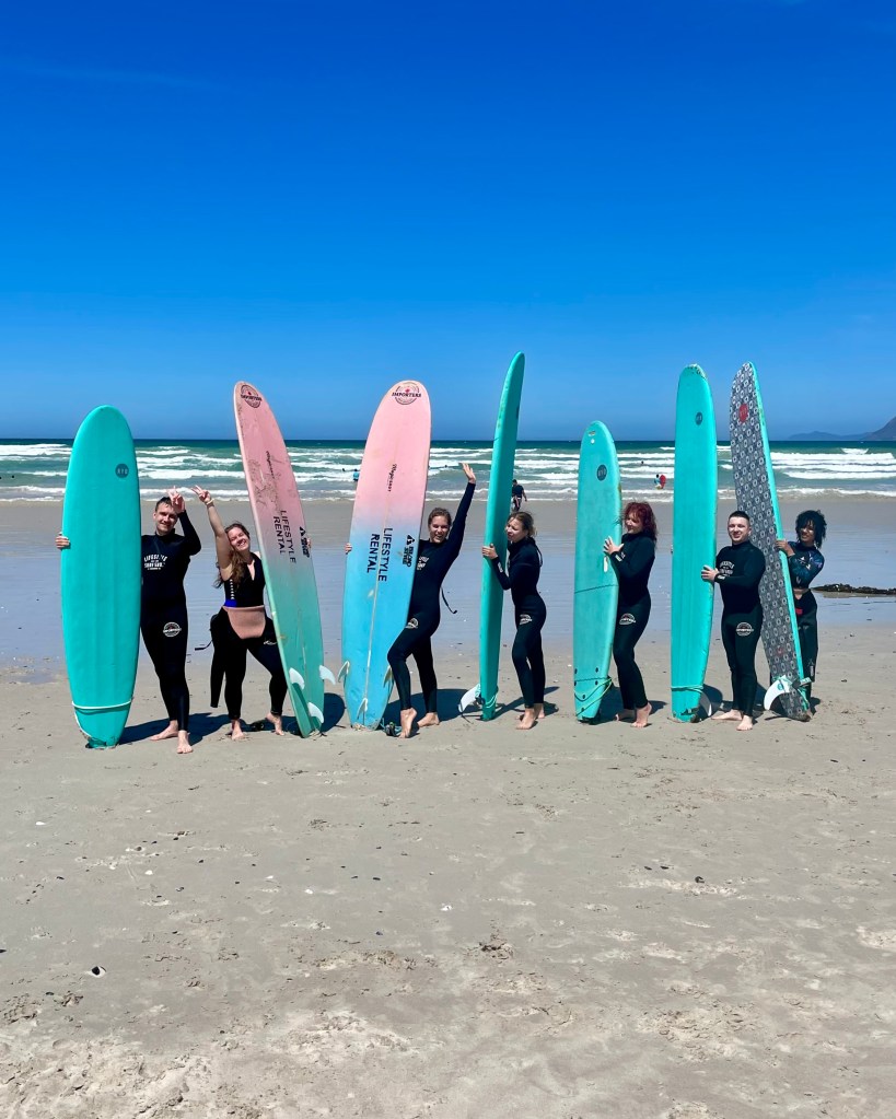 A group of beginner surfers at a group surf lesson, posing for a picture with their surfboards at Muizenberg beach in Cape Town, South Africa