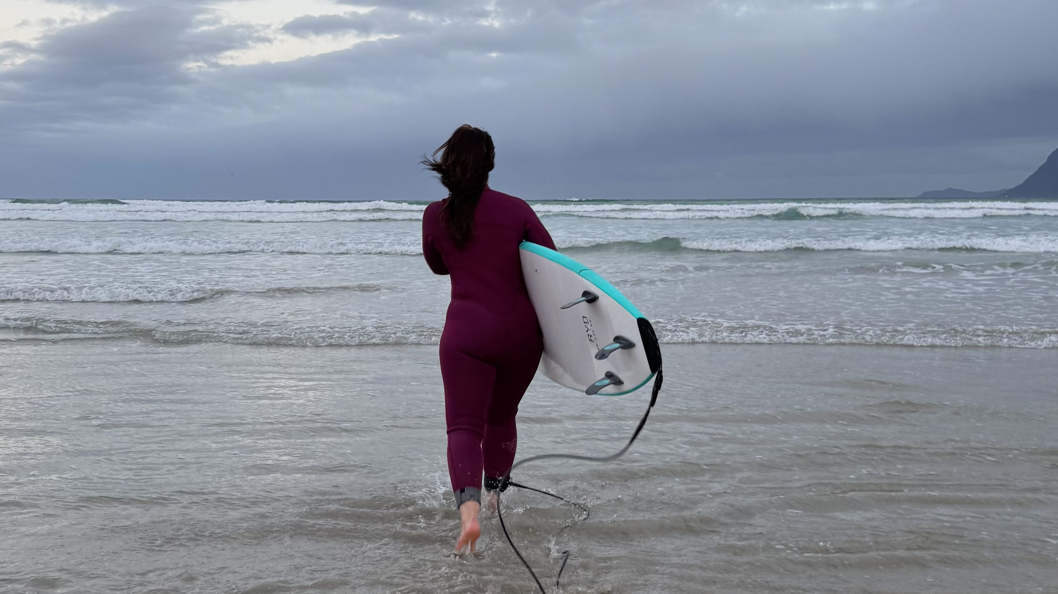 Female Surfer wearing a wetsuit and carrying her surfboard, going into the water at Muizenberg beach
