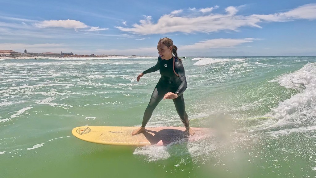 A female surfer standing on the surfboard smiling and riding the wave during her surf lesson in Muizenberg Cape Town